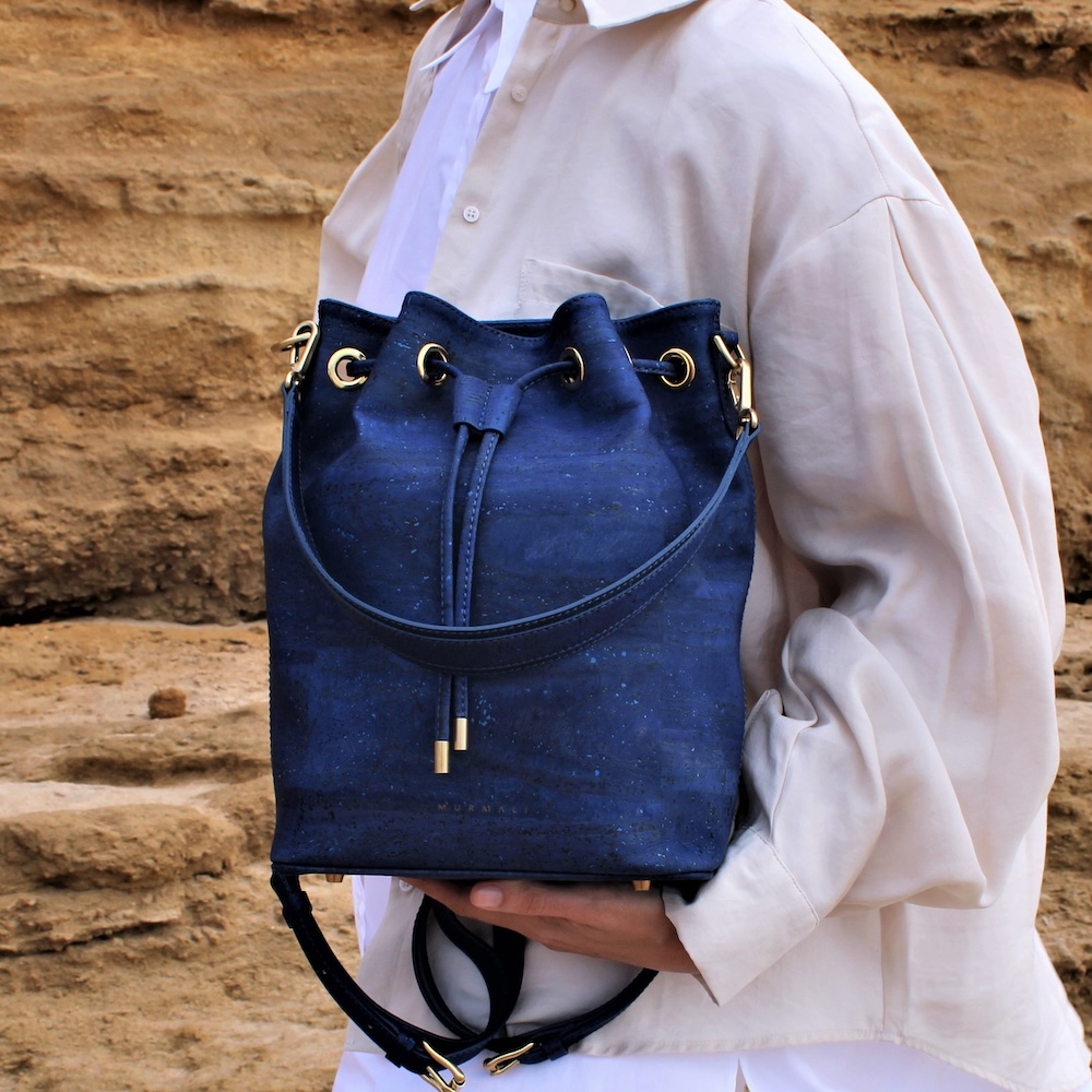 The photo is meant to depict exampe of what is vegan leather: a blue, cork leather bucket back that a women dressed in white is holding up